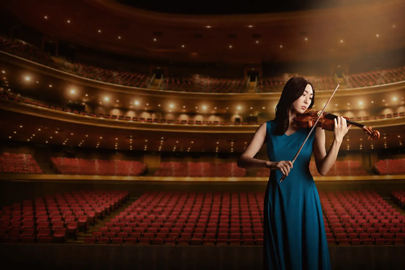 A violinist in a teal gown performs on a concert-hall stage