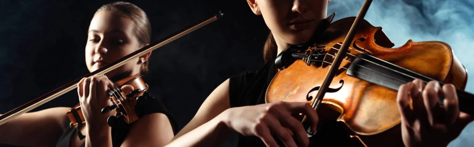 Two violinists perform in a dark, moody setting